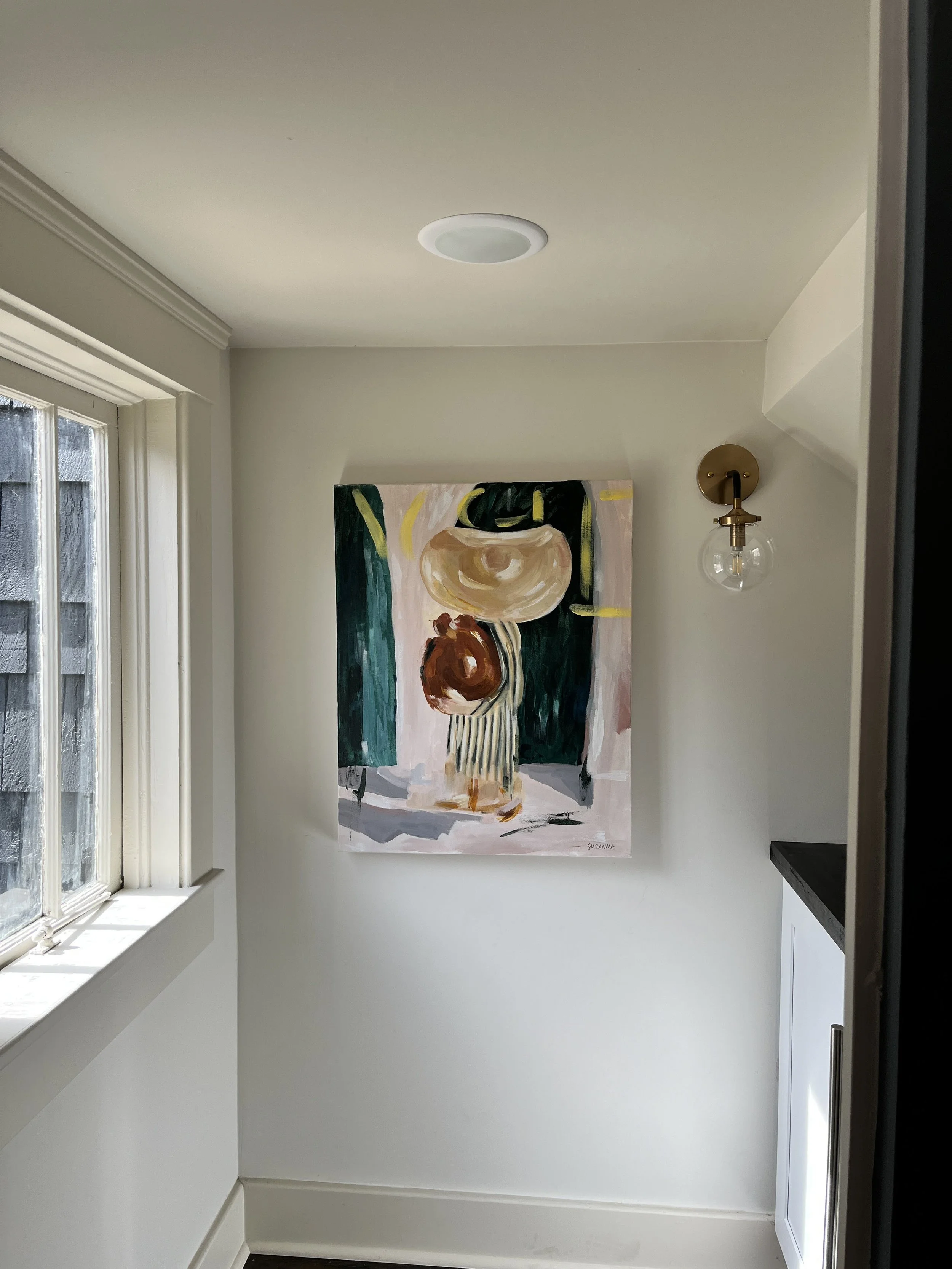 An impressionist painting of a woman wearing a large hat and carrying a vase hangs in a well lit hallway.