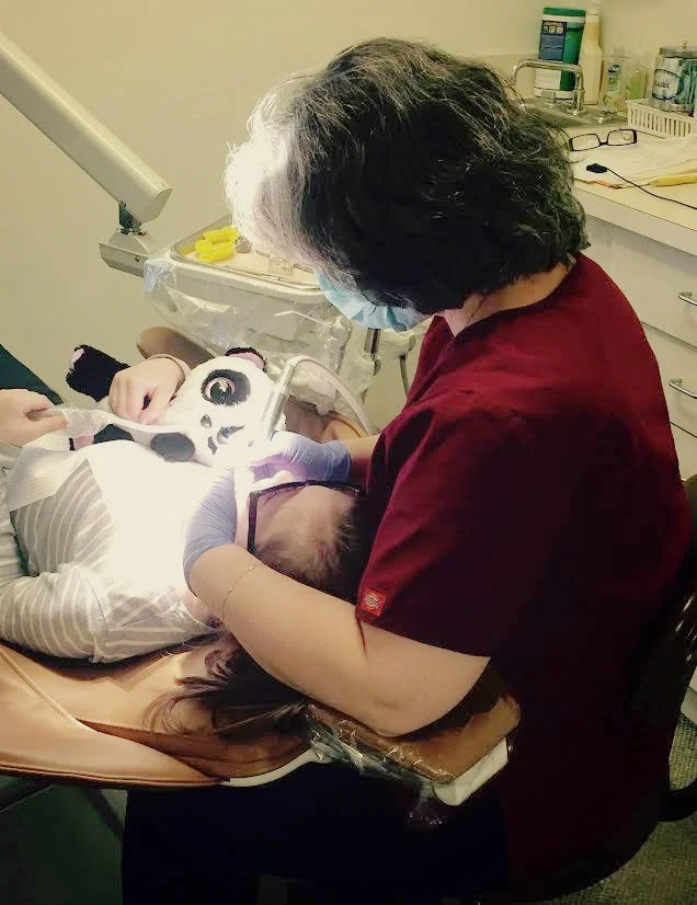Dr. Viera with a patient holding a stuffed panda during a cleaning. 
