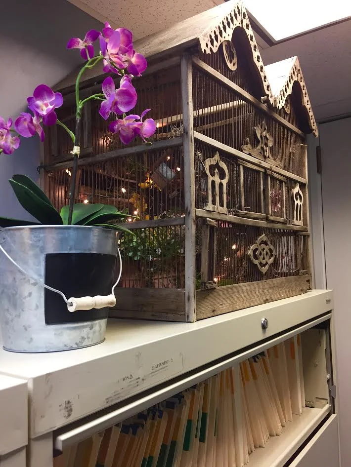 Decorated birdhouse with orchid on top of filing cabinets.