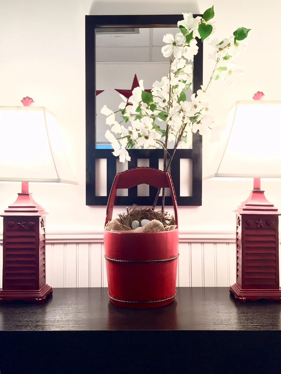 Entrance table with mirror, red wooden bucket with white dogwood flower, and lamps to match.