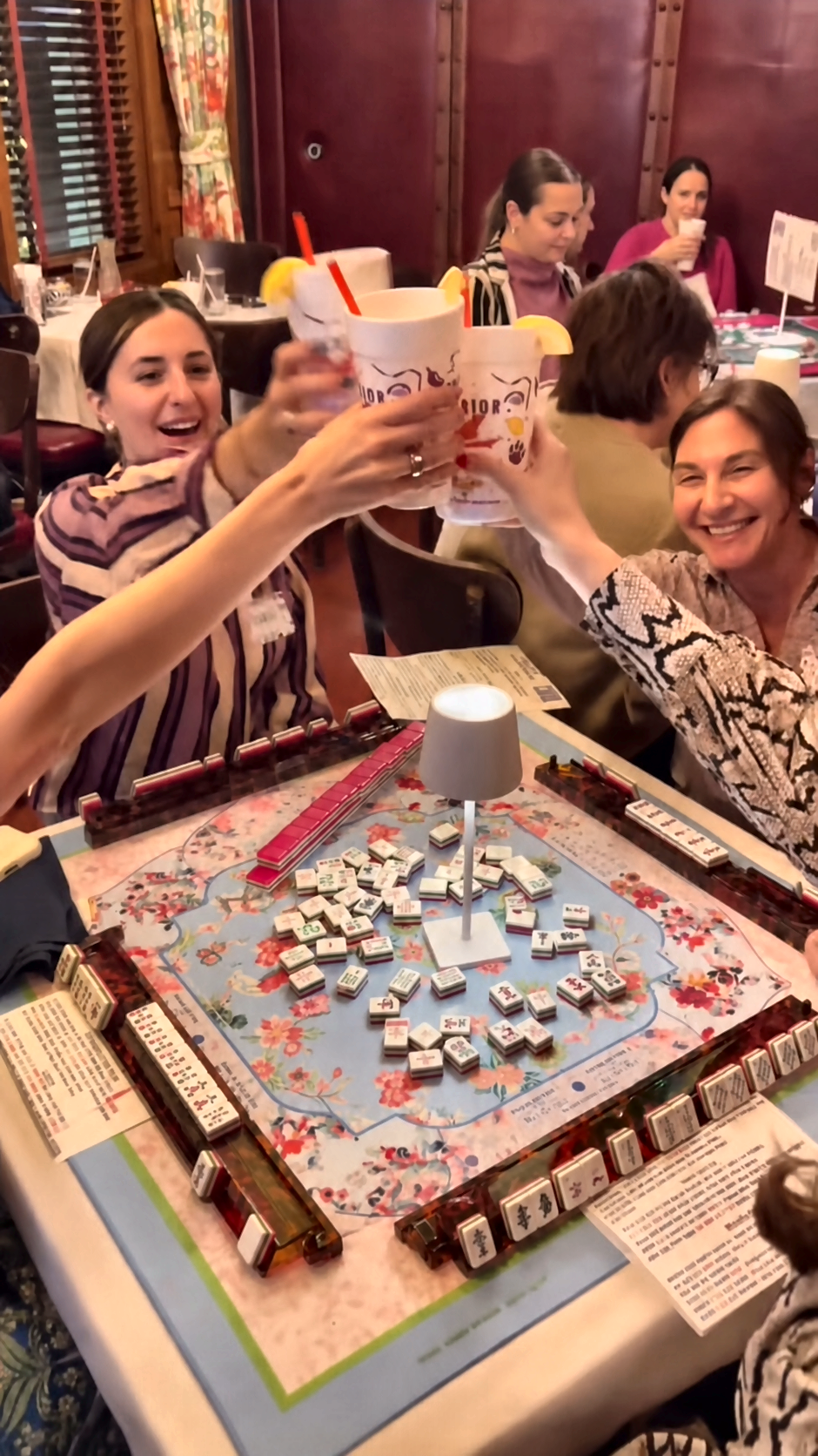 Mahjong students toast together around one of Marcy Maurer’s colorful game tables.