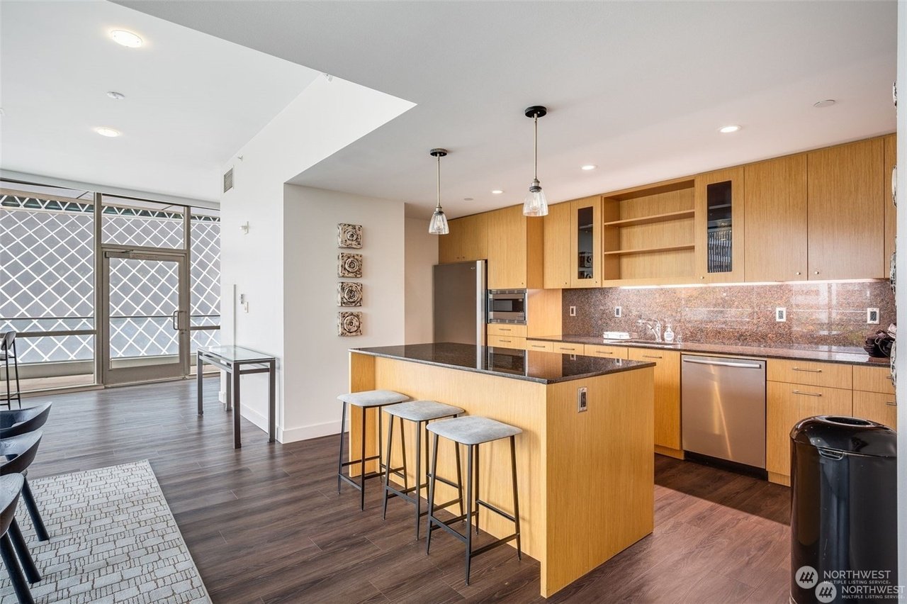 Modern kitchen interior with wooden cabinets, granite countertops, stainless steel appliances, and bar stools.