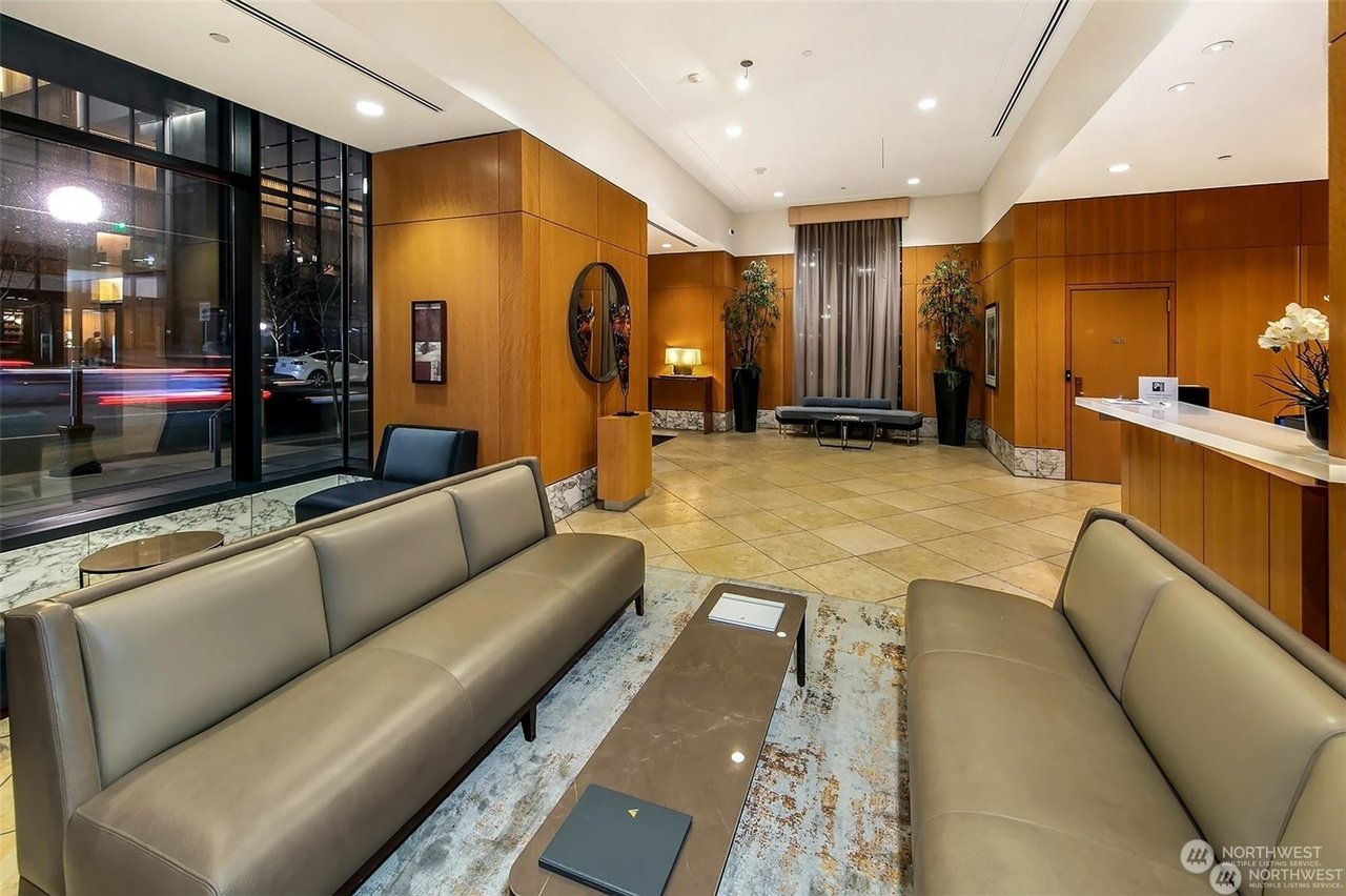 Modern hotel lobby with beige sofas, large windows, a reception desk, and decorative plants.