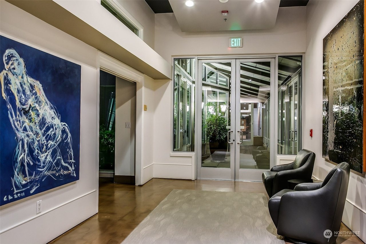 Modern lobby area with abstract artwork, glass doors, and two black leather chairs.