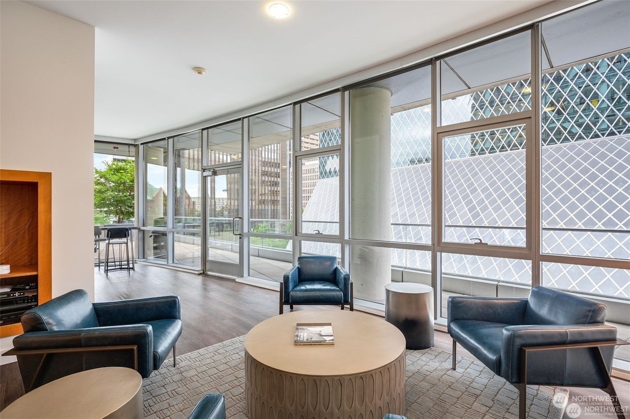Modern lobby with large windows, blue chairs, round table, and a view of city buildings.