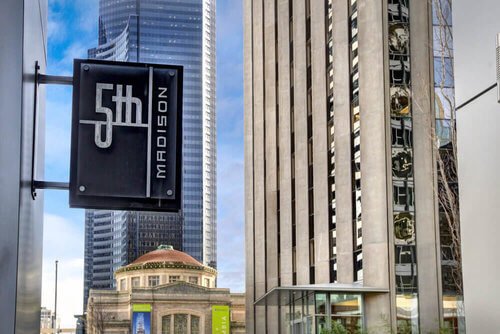 Street view with "5th and Madison" sign, modern skyscrapers, and historic architecture in an urban city setting.