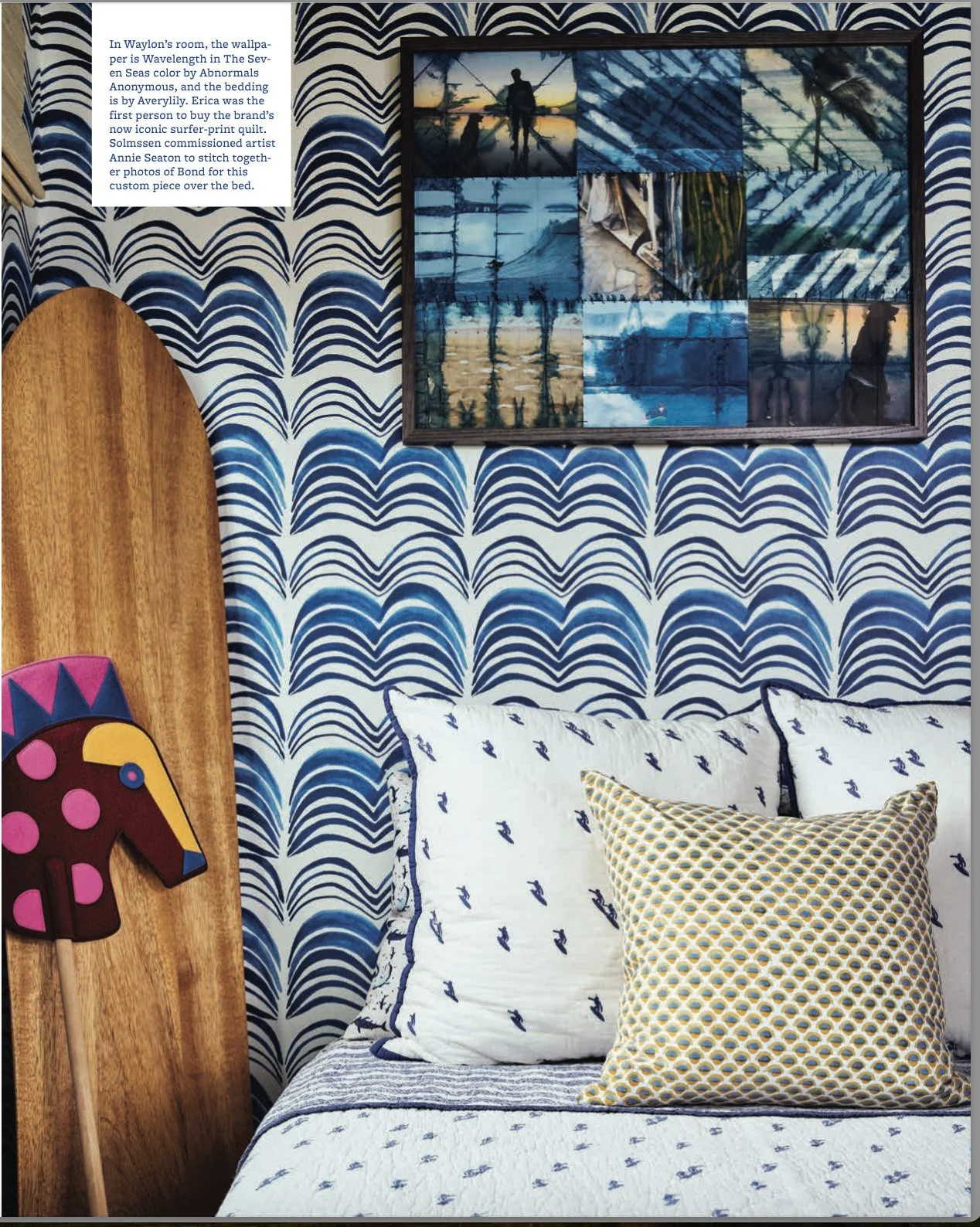 A bedroom with a blue and white patterned wall, three pillows on the bed with nautical and geometric designs, a framed collage of beach and nature photos, and a wooden decor piece resembling a horse with a colorful mane leaning against the wall.