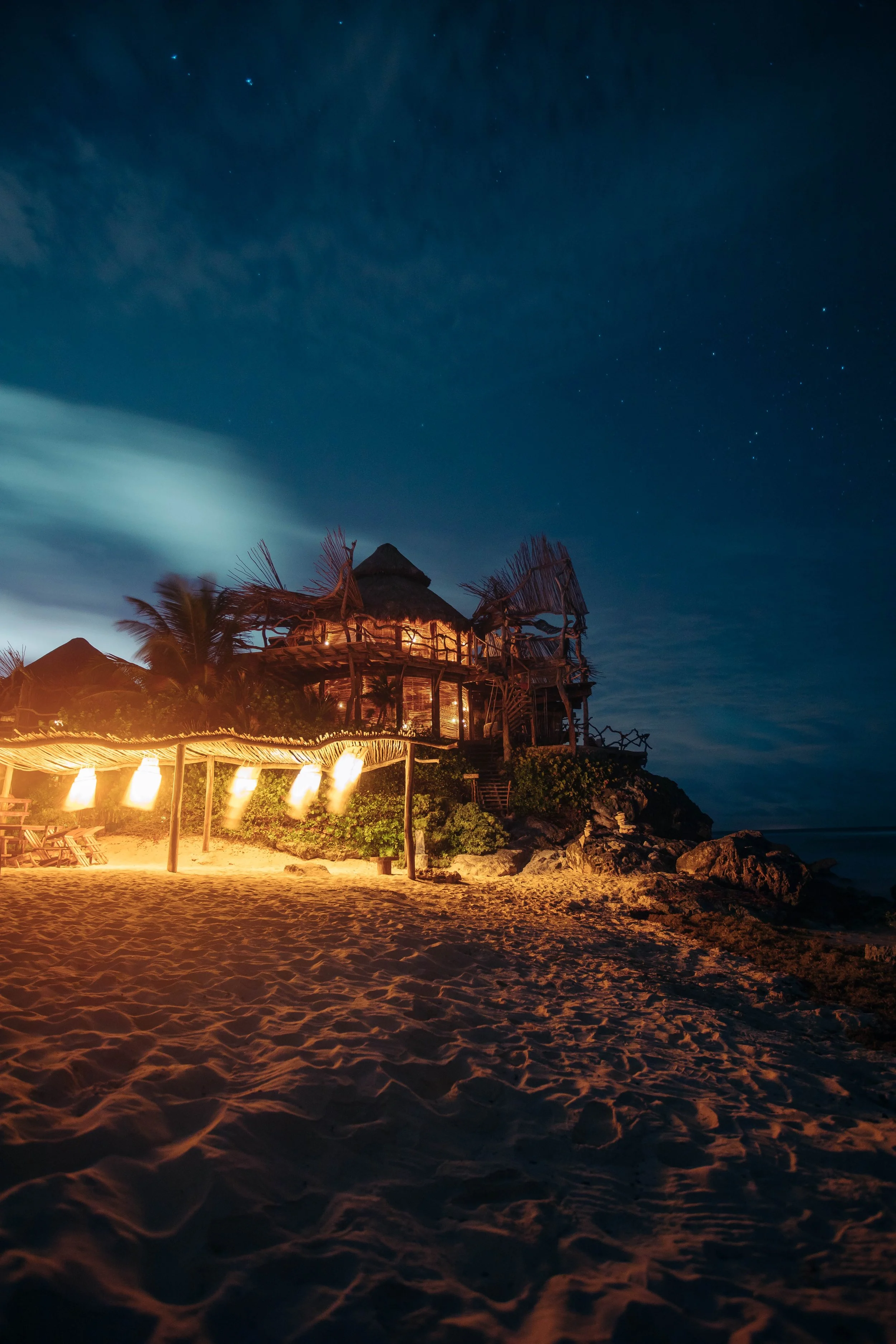 tiki style hut hotel in the sand on a beach at night