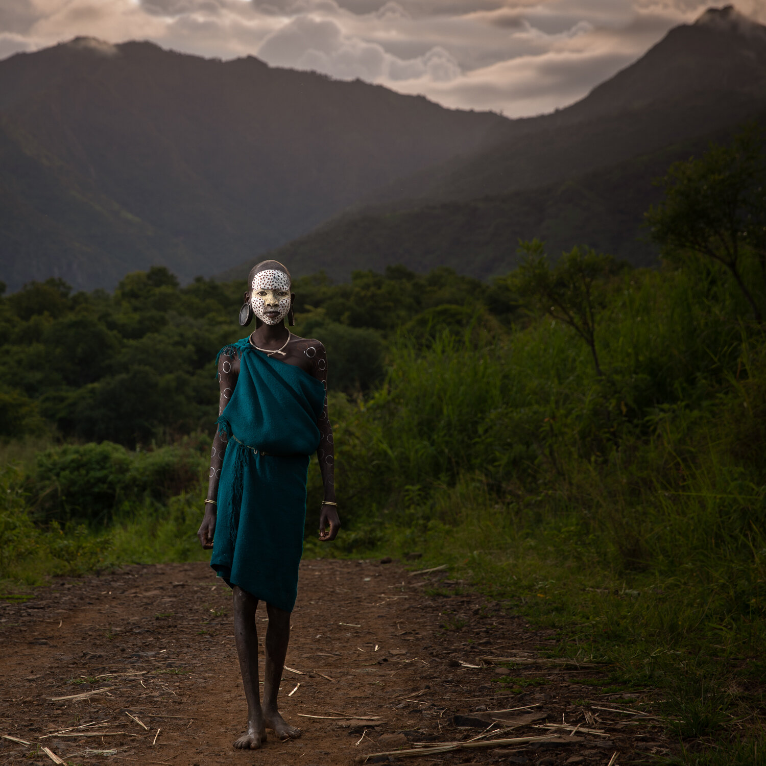 A young Suri   girl walks towards her village as the sun goes down.&nbsp;The  Suri tribe  is very creative with body painting and decoration. 