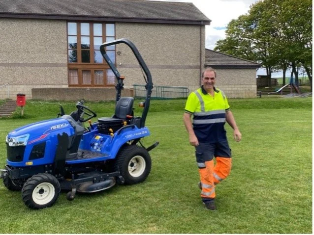 A man in a high-vis jacket standing next to a sit-on mower