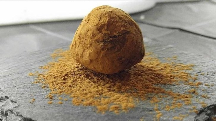 A single Bittersweet truffle dusted in cocoa powder on a gray slate serving tray