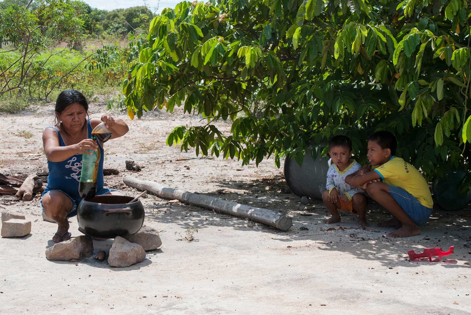  Most families make black tucupi in the village, and have their own manioc plantations. The sun is searing hot at midday. This mother decants black tucupi into fizzy drink bottles.  Photo © Tina Leme Scott    