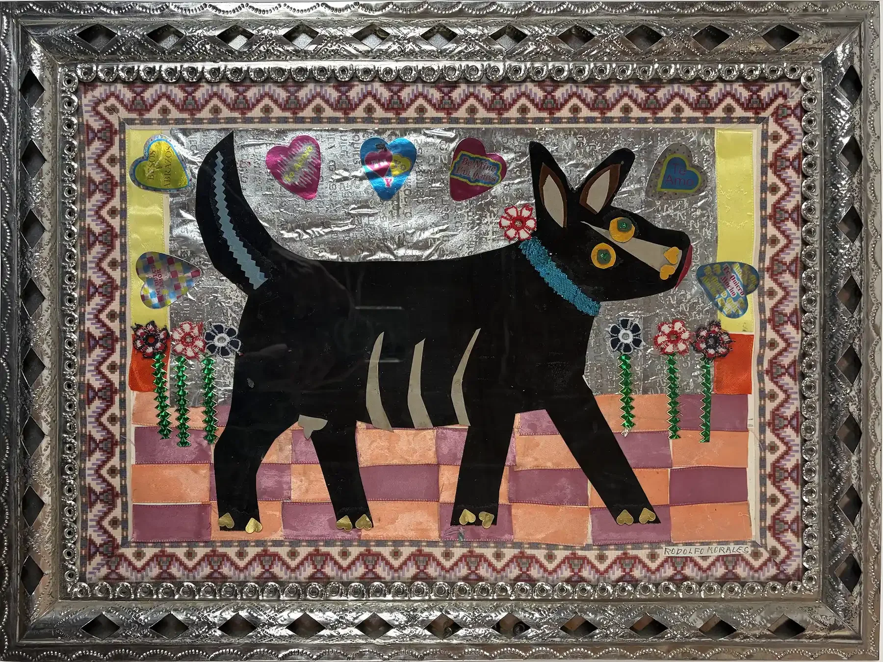 Mixed-media collage by Rodolfo Morales of a black dog with hearts and flowers, on a foil background, in a hand-tooled tin frame stamped Tirso Cuevas.