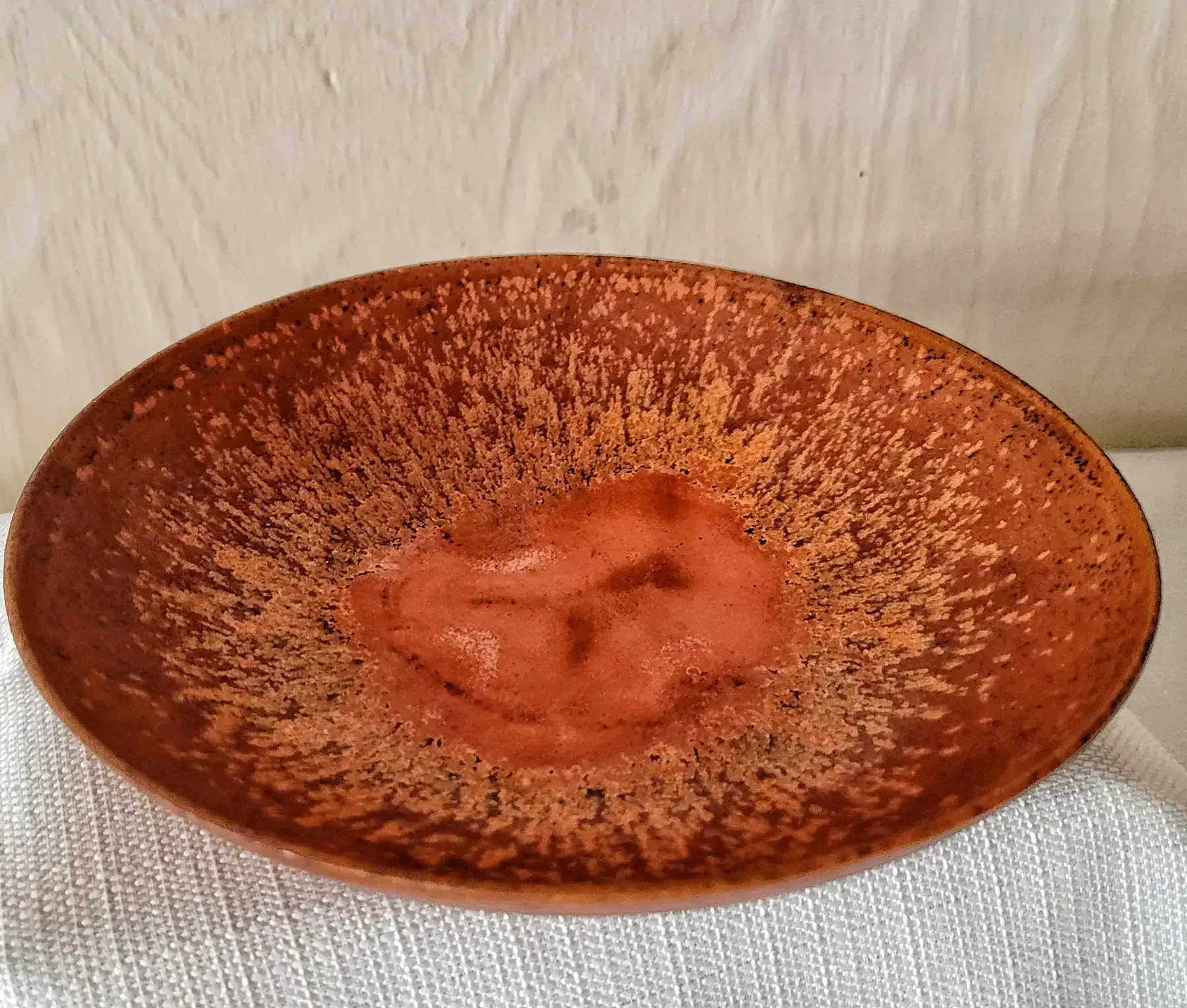 Shallow Otto and Gertrud Natzler bowl in crater-red glaze with speckled, volcanic texture.