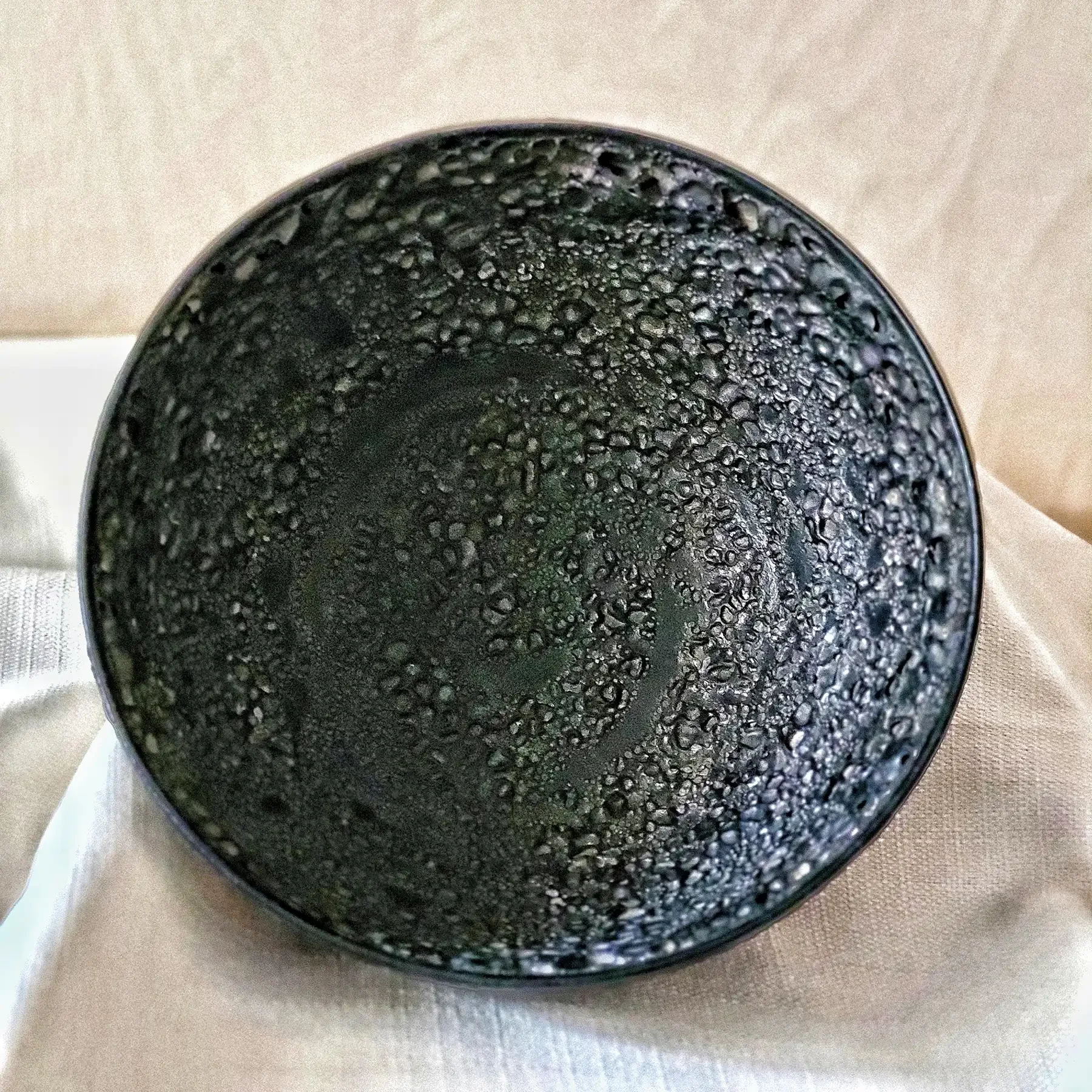 Top view of Natzler Black Lava bowl with dense cratered volcanic glaze pattern.