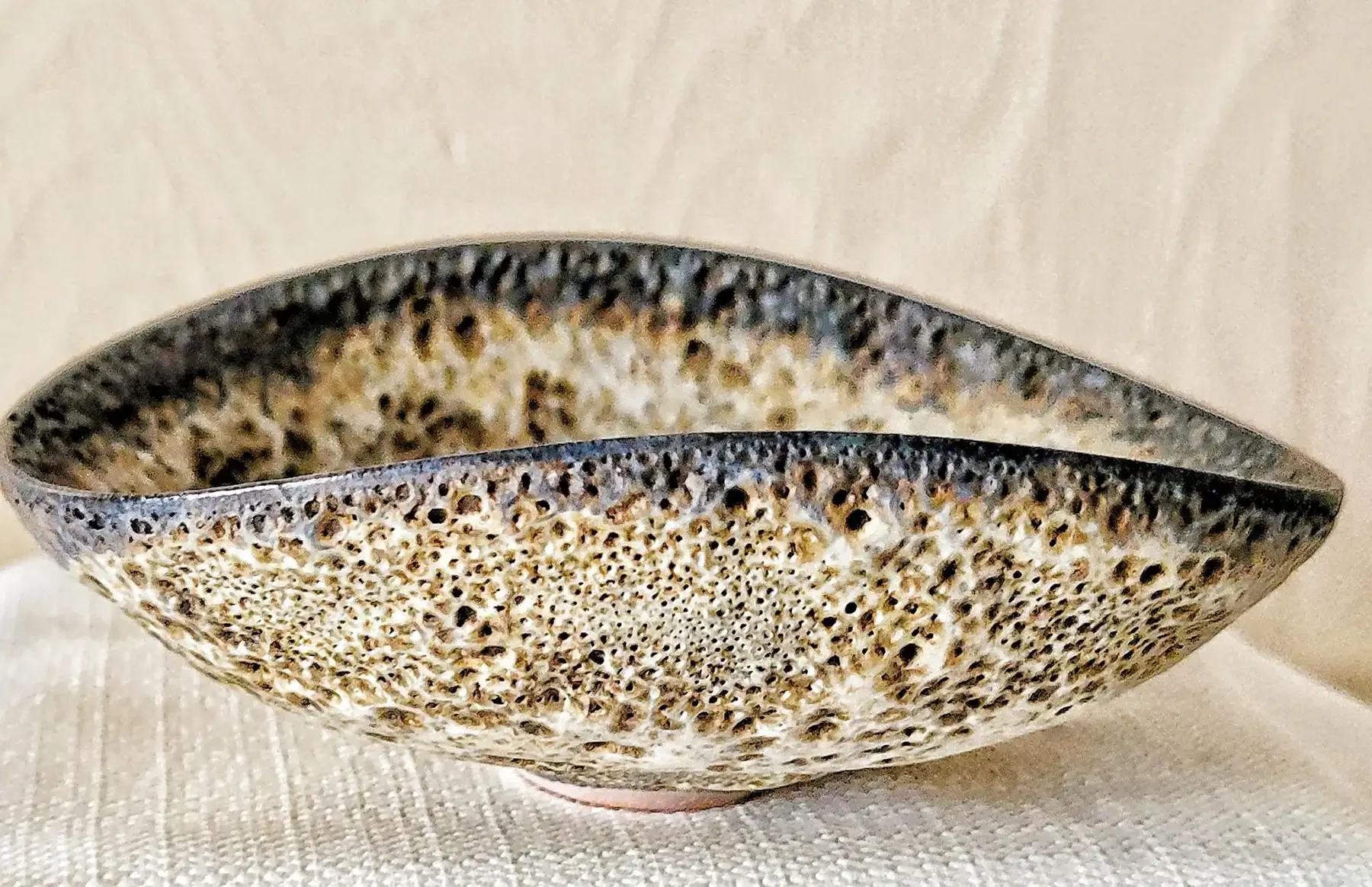 Side view of Otto and Gertrud Natzler stoneware bowl with cratered white lava glaze and asymmetrical rim.