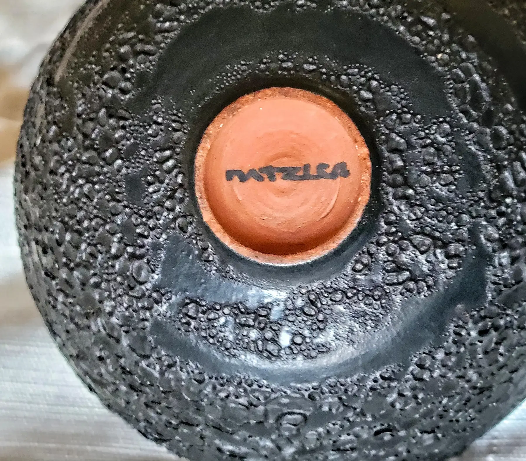 Base of Natzler bowl showing “Natzler” signature and cratered Black Lava glaze texture.