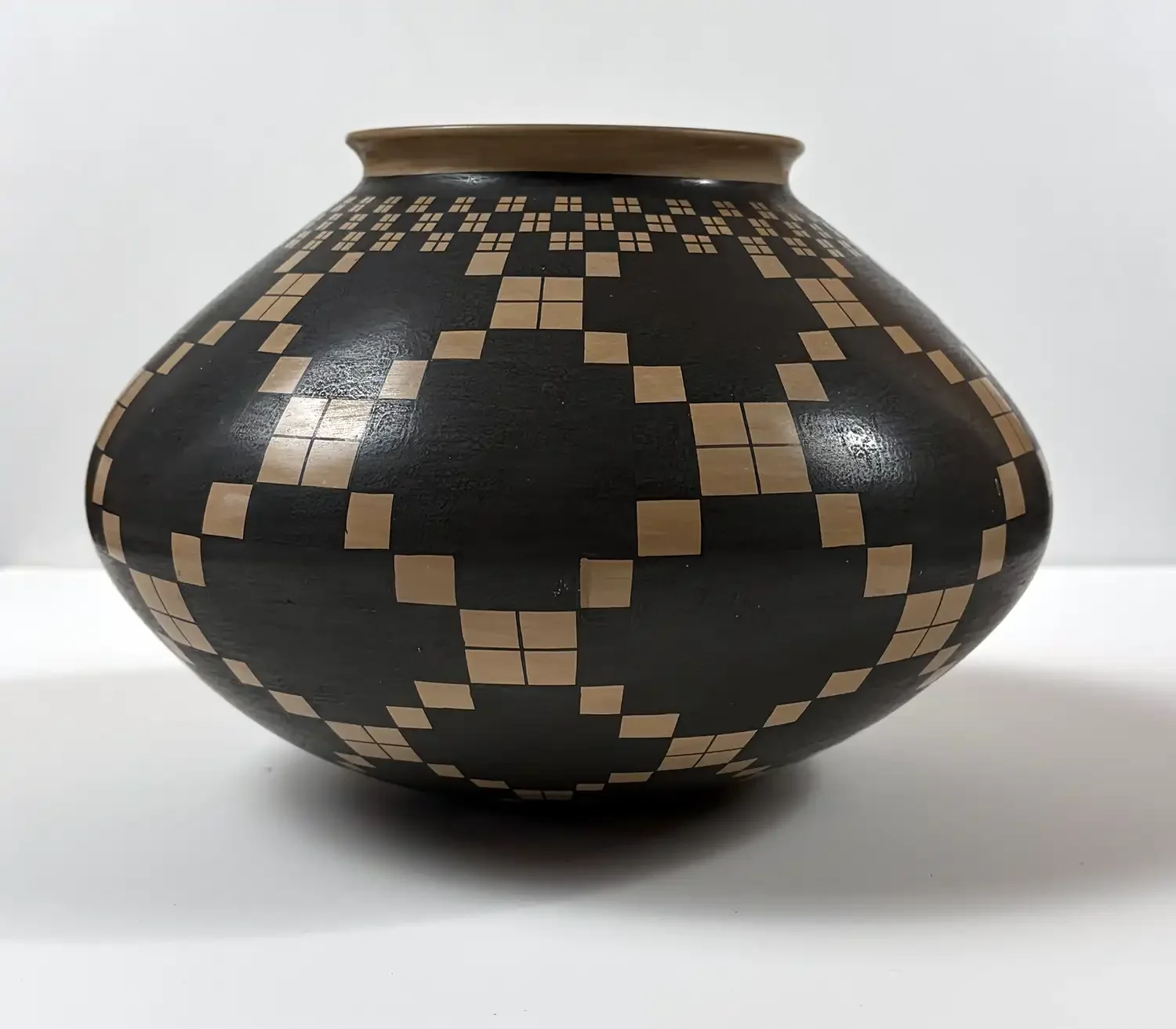 Black-on-white geometric Mata Ortiz olla by Juan Quezada with interlocking stepped and square-grid patterns.