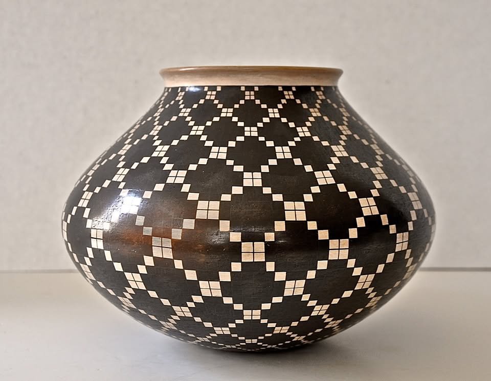 Black-on-white geometric Mata Ortiz olla by Juan Quezada, featuring interlocking square-grid patterns and a radiating starburst design on the top.