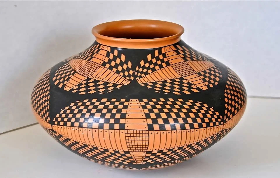 Orange-and-black geometric Mata Ortiz olla by Juan Quezada, featuring radiating checkerboard and curved grid patterns on a rounded, stone-burnished form.