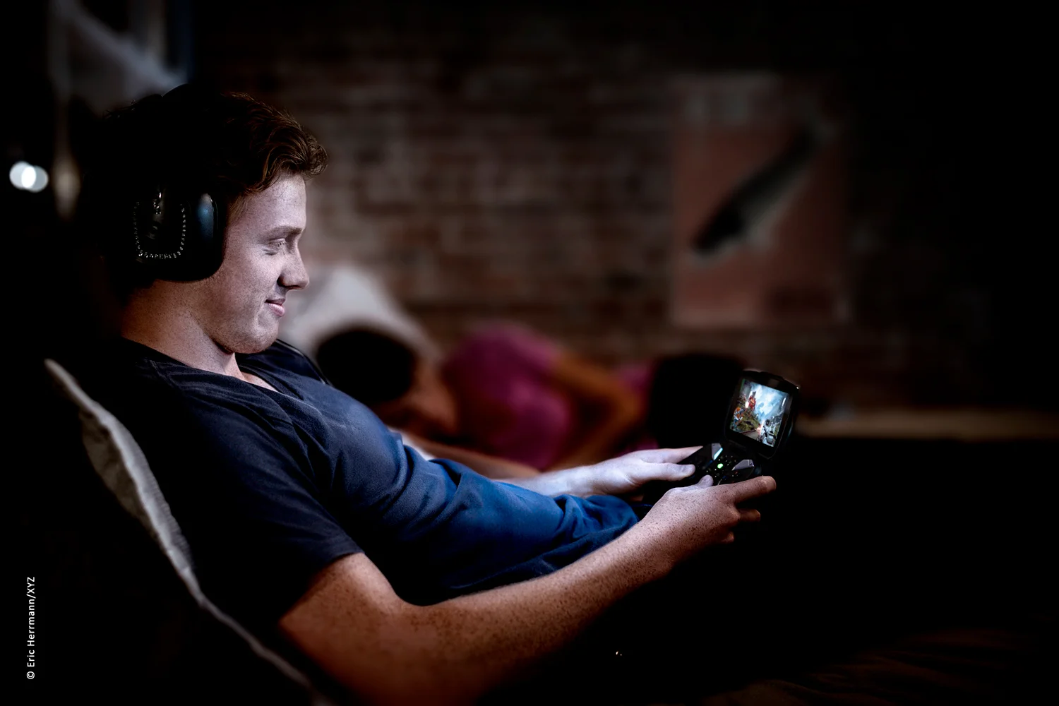 Photo of a young man sitting in bed at night wearing headphones quietly playing avideo game on his Nvidia Shield