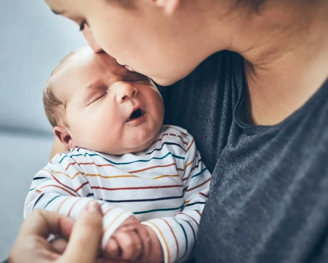 A woman kissing a sleeping baby on the forehead.