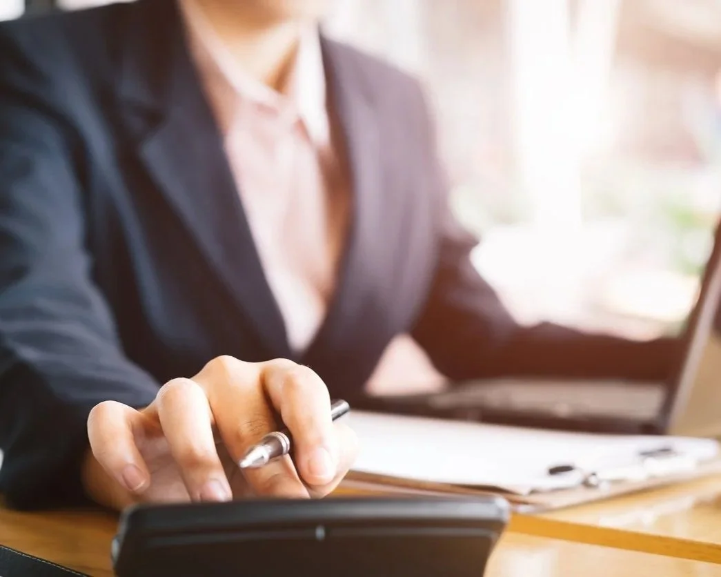 A person in a dark blazer is using a stylus on a tablet at a desk, with a laptop and papers nearby.
