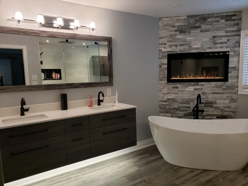 Modern bathroom with double vanity, large mirror, fireplace, and freestanding bathtub.