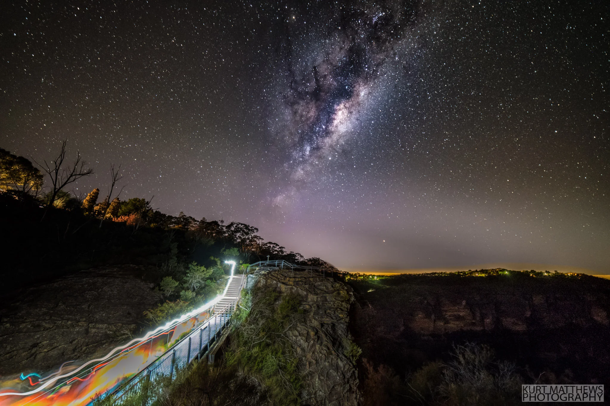 Runners pass over a cliff top bridge below the milky way.