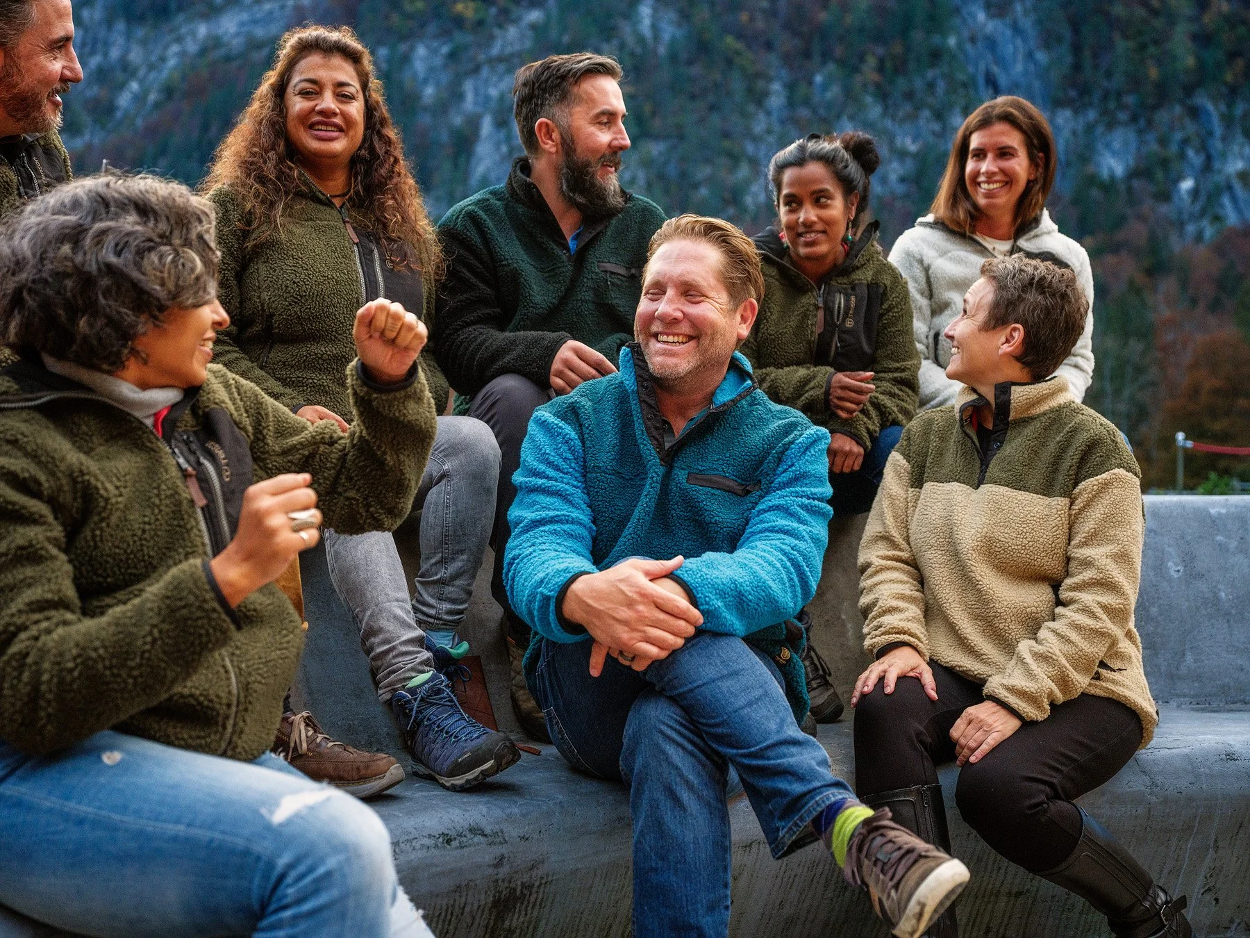 Jake laughing in center of diverse group at fire pit; mountains behind.jpg