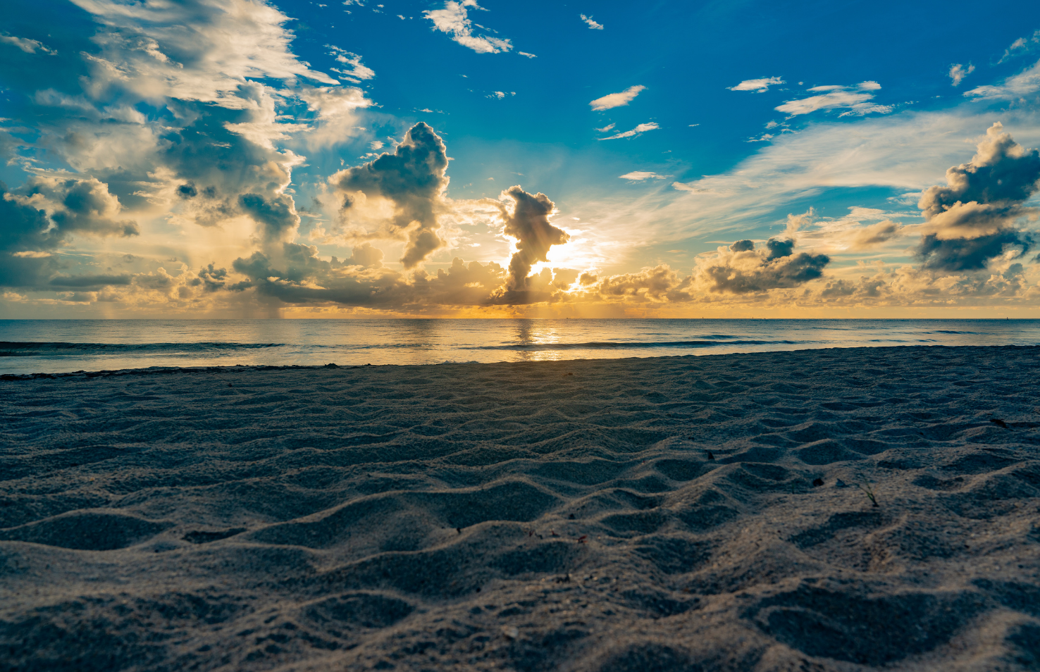 Sunrise over a Treasure Coast beach with ocean waves, sandy shoreline, and dramatic coastal clouds.