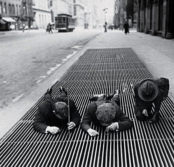 Scouring for change through a street grate during the Depression, New York, 1930.