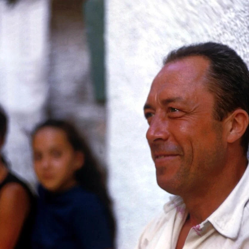 This is my favorite photograph of Albert Camus. Usaully portrayed in black &amp; white in the intellectual grey of Paris, here he is standing, tanned, against the glimmer of a white wall &amp; smiling eyes in presumably his native land of Algeria, where so many of the French intellectuals before and after Camus where born &amp; lived as children.