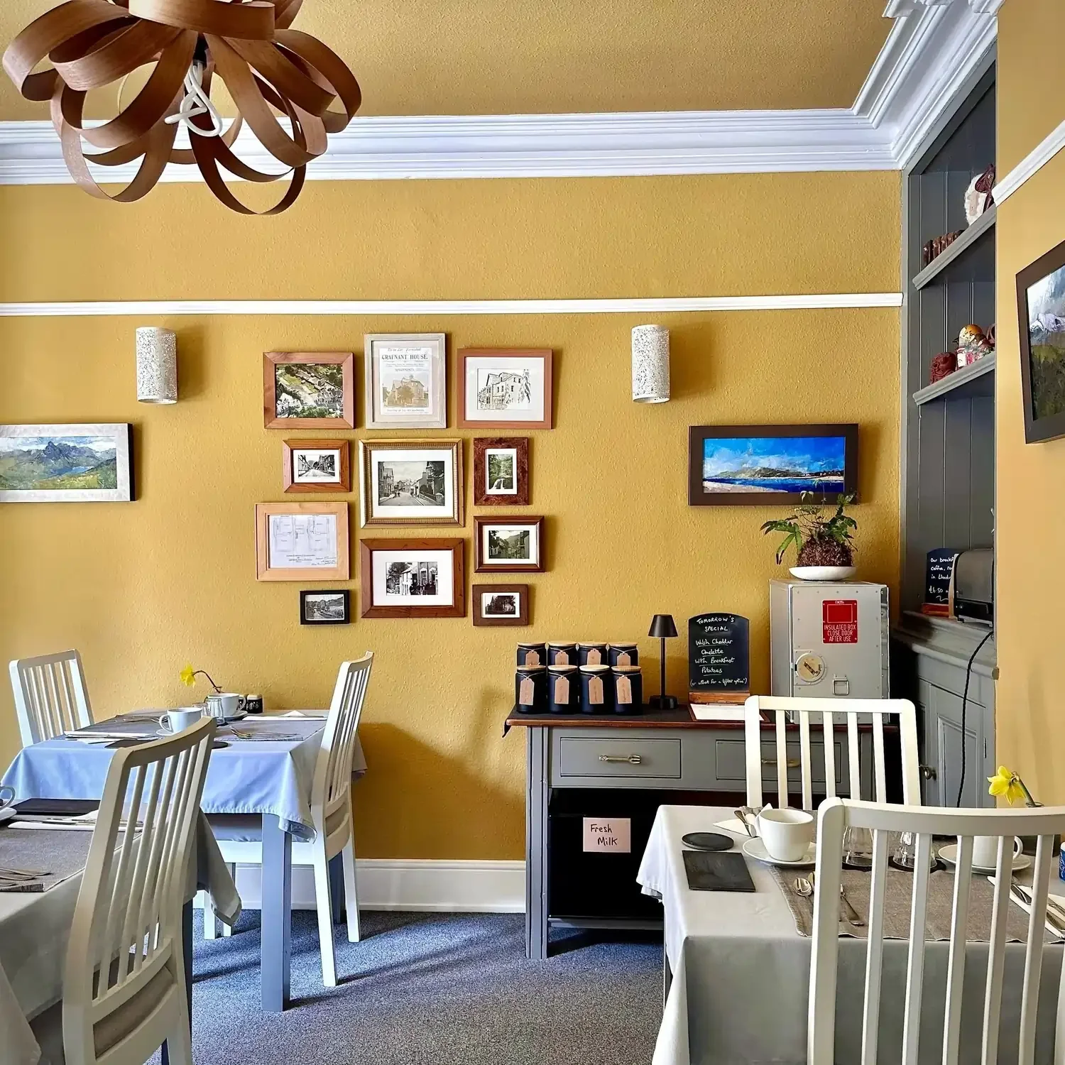 The dining room at Crafnant House Bed and Breakfast in North Wales, with yellow painted walls, an ornate light, and tables and chairs