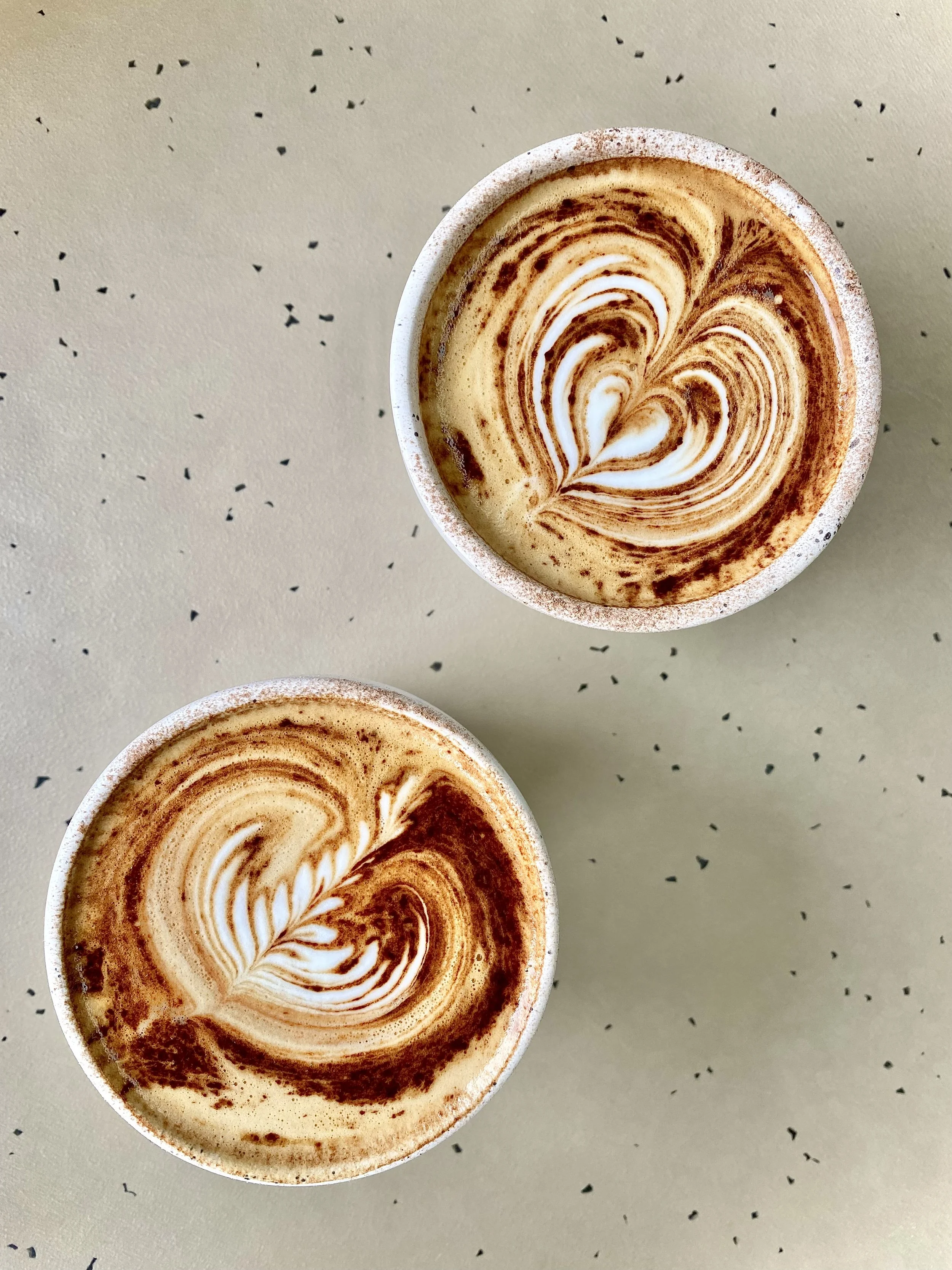 Two coffee cups on a table with pretty latte art on top