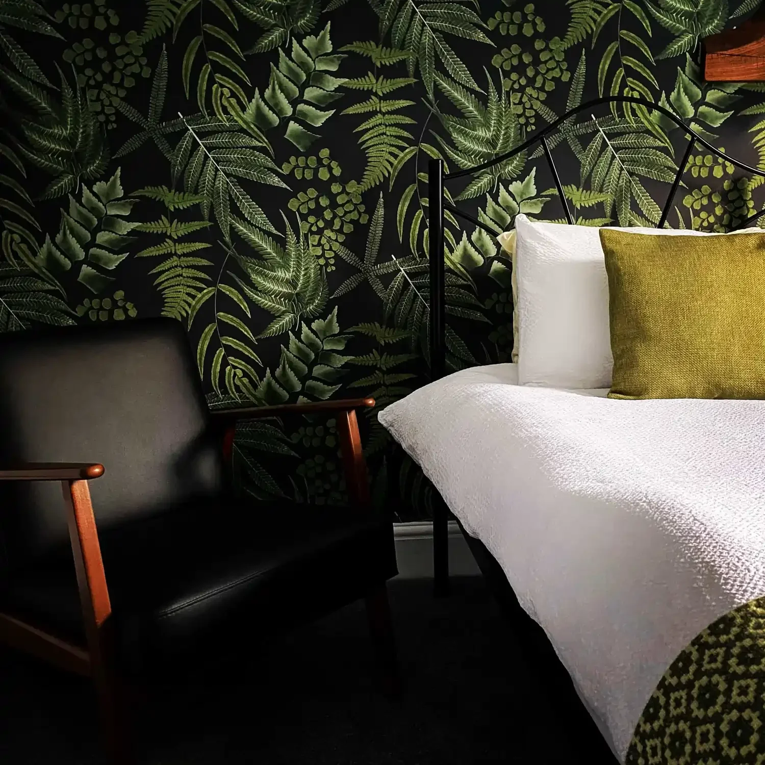 Bedroom in a B&B featuring a bed with white linen against wallpaper with a foliage design, and a chair next to the bed