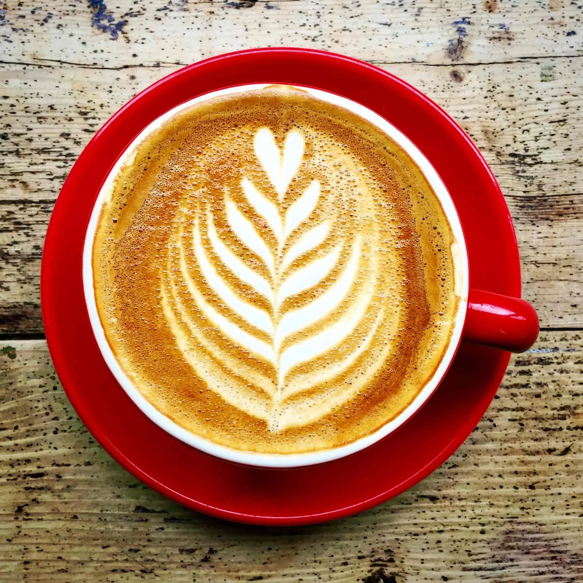 A cup of coffee on a red saucer seen from above on a wooden table