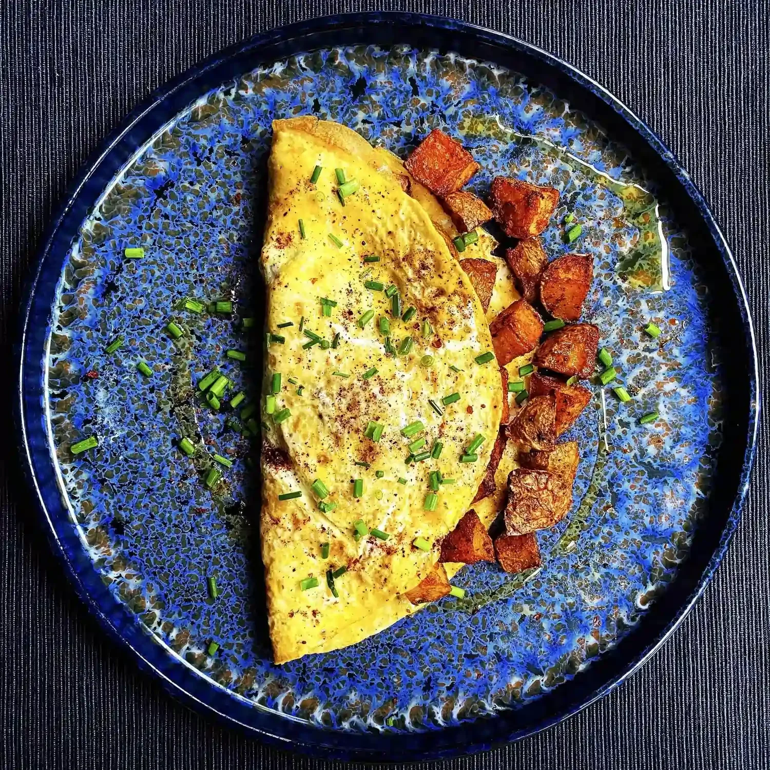 A blue plate on which is a yellow cheese omelette and roasted potatoes