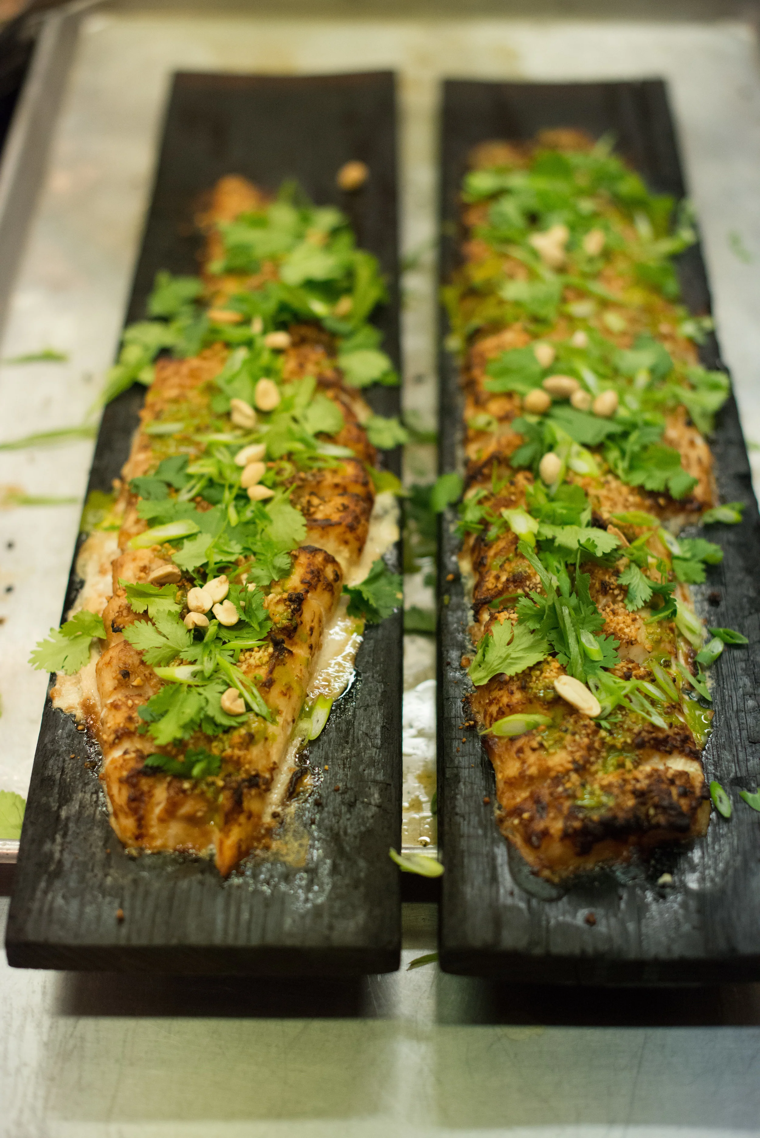 Photo by Kristen Loken Cedar Plank Roasted Miso Peanut Butter Fish Ingredients · 4 7-8 oz fish fillets, skin on (helps fillet to stay together) · Green onions, for garnish (optional) For Peanut Butter & Miso Glaze: · 3 tbsp hot water · 2 tbsp peanut butter, unsalted · 1 tbsp white miso paste · 1 tbsp rice vinegar · 1 tbsp soy sauce · 1 tbsp ginger, grated · 1 garlic clove, crushed Directions 1. Get fillets fabricated and ready. 2. In a small bowl, whisk together glaze ingredients and pour over the fish. Release as much air as possible and seal the bag. Marinate refrigerated for at least 30 minutes or maximum overnight. 3. Preheat oven to 400 degrees F. 4. Place fish fillets on cedar planks, leaving 1.5" - 2" space in between them. 5. Spoon remaining marinade on top of the fillets. Cook for 12-15 minutes and then broil on Low until brown crust forms on top. 6. Serve immediately garnished with chopped green onions, shaved roasted peanuts and a drizzled of green peanut oil. Courtesy of The Culinary Institute of America - St. Helena, California