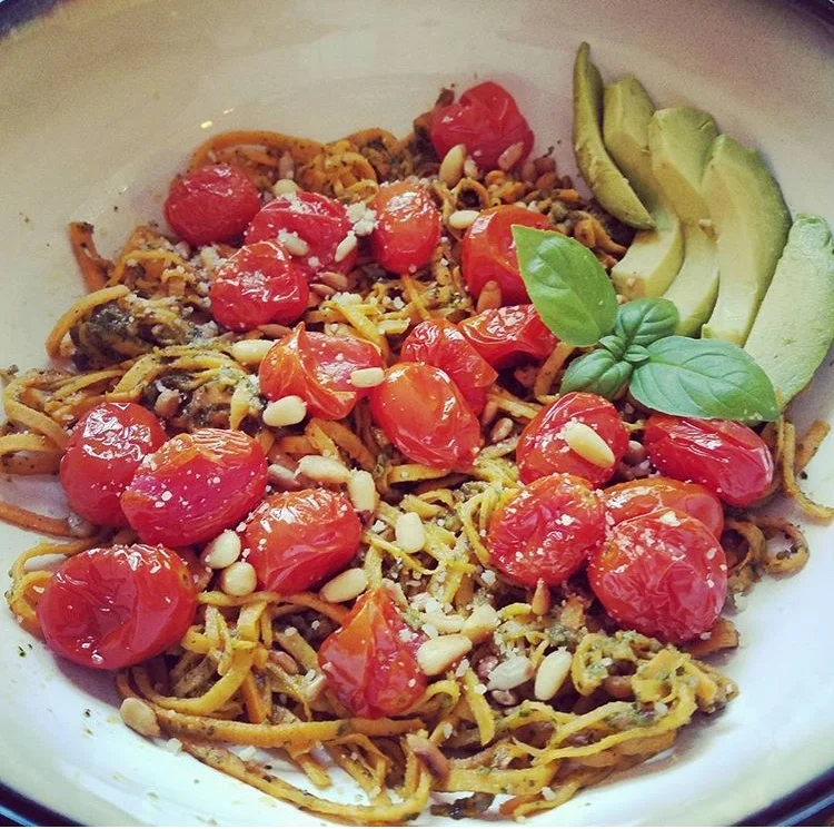 Ingredients: - 1 ¼ cups of pine nuts (1/4 c. for topping) - ¾ cup Oliver Farm Pumpkin Oil - The juice of 1 lemon - 1 cup basil leaves packed (equals 2 bunches with stems) - ½ tsp salt - ¼ tsp pepper - ¾ cup vegan parmesan cheese - 1 Tablespoon Pumpkin oil (for pine nuts) Directions: - In a nonstick sauce pan add the 1 ¼ cup of pine nuts and 1 Tablespoon Pumpkin oil. Stir continually for 3-5 mins on medium high heat until the pine nuts are golden brown. Set aside to cool. - Then in a food processor add basil, lemon juice, salt, pepper, parmesan cheese, and 1 cup of cooled pine nuts. Save the other ¼ cup for topping to prepared dish. - Pulse all ingredients until it is a course ground, while the processor is on slowly drizzle the pumpkin oil in. If it seems too dry and is not combining smoothly continue to drizzle in pumpkin oil until desired consistency is achieved. Sweet Potato Spirals with Grape Tomatoes and Pesto: - In the above picture I spiraled a sweet potato and tossed them in a nonstick pan over medium heat along with 1 Tablespoon pumpkin oil pesto to heat together. - While this was heating and combining, I roasted 1 pint of grape tomatoes and 3 garlic cloves in 2 teaspoons Oliver Farm Benne Oil, ¼ teaspoon salt and pepper at 400 degrees for 8-10 minutes or until golden brown. - I plated the sweet potatoes with pesto, then added a generous amount of roasted grape tomatoes and garlic to the top along with a sprinkling of vegan parmesan cheese and remaining toasted pine nuts. Photo and recipe by Carla Poff