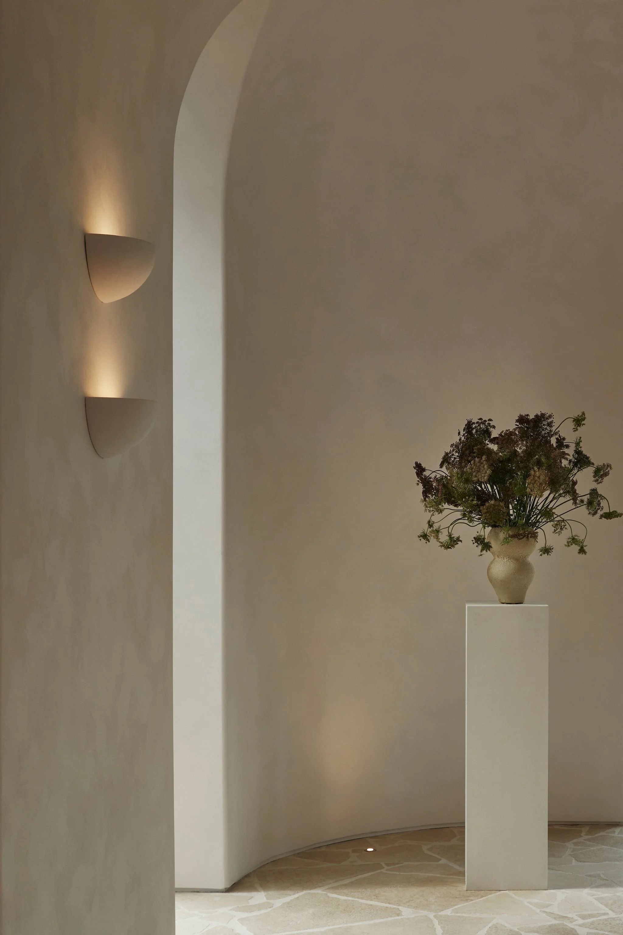 Curved plaster architecture, integrated wall lighting and floral display inside the Lune 1860 barn.