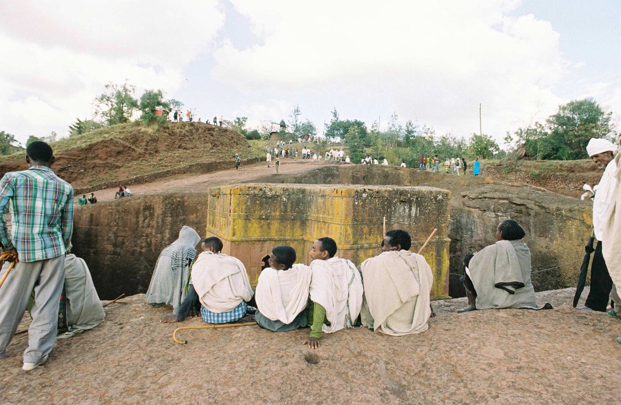  A moment to relax, pilgrims sit along the edge of the earthen wall that surrounds the rock-hewn Church of St. George.&nbsp; 