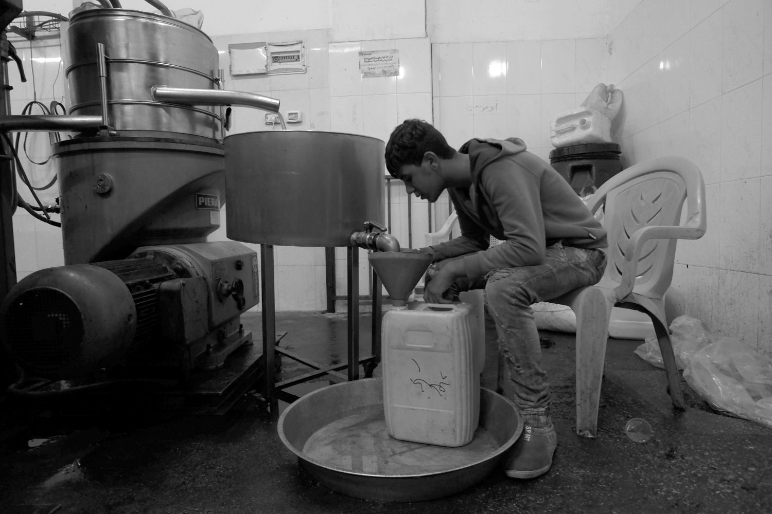Hakam, Mr. Abdalhade's young worker, sits next to the press bottling today's harvest.