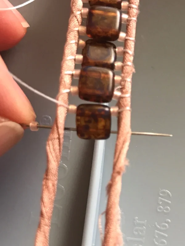 8. Thread your needle through the second hole of the two-hold bead. It's hard to see in this photo, but my needle really is through the brown bead.
