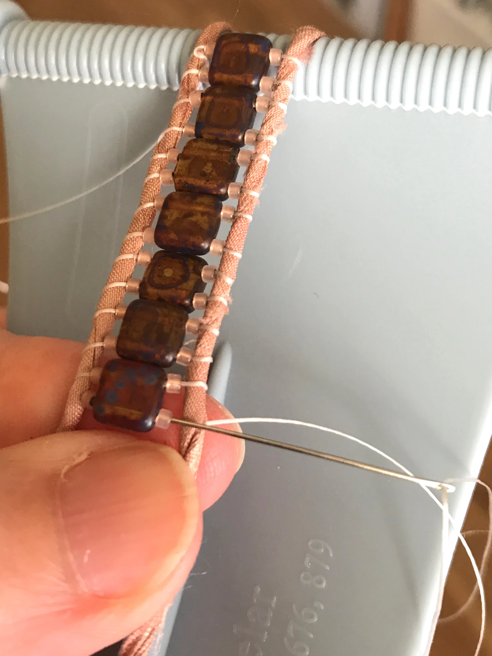 10. Use your finger again to nestle everything nicely between the ribbon strands. Bring your needle up and to the top of the work and thread it back—right to left—through all three beads with the needle remaining on top of the left strand.