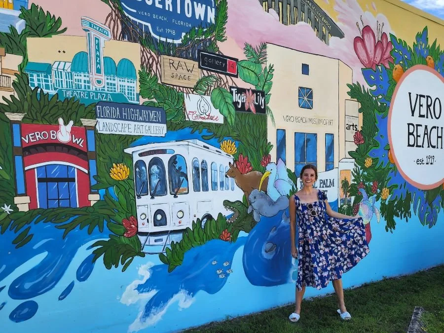 A woman twirls in a dress in front of a colorful mural for Vero Beach Florida.