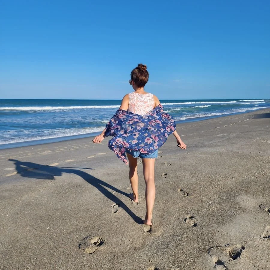 A woman walks on the sand toward the water on a Melbourne girls getaway in Florida.