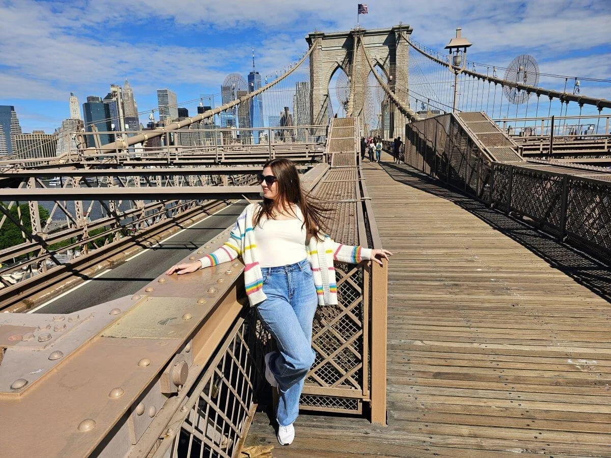 A woman stands on a bridge with a New York attraction passes