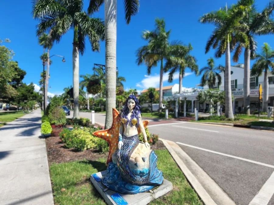 A statue of a mermaid under palm trees in downtown Venice Florida.