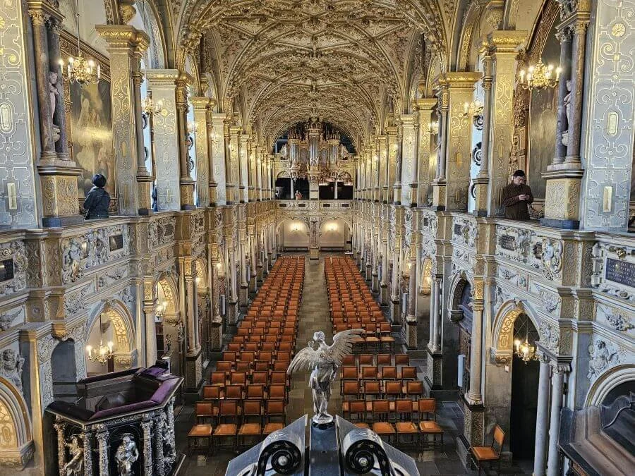 A chapel inside Frederiksborg castle with white and guilded walls, seats down the center, and a huge organ on the back wall.
